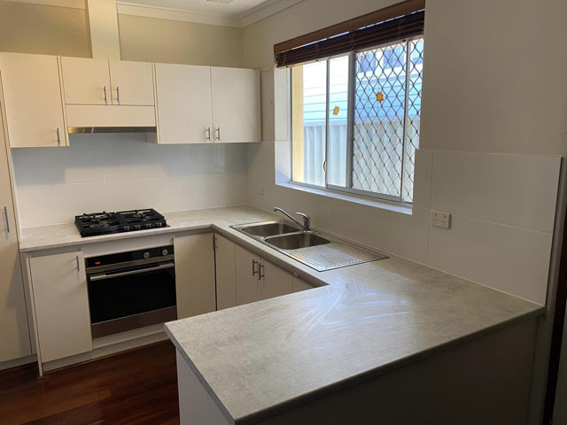 Same kitchen after renovation: grey benchtops, white cupboards and gas cooktop