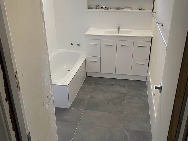 Bathroom with white bath, white vanity and dark grey floor tiles