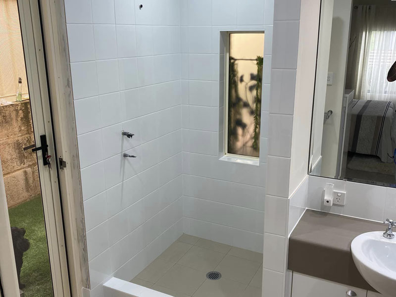 White-tiled shower recess with a narrow window beside a basin