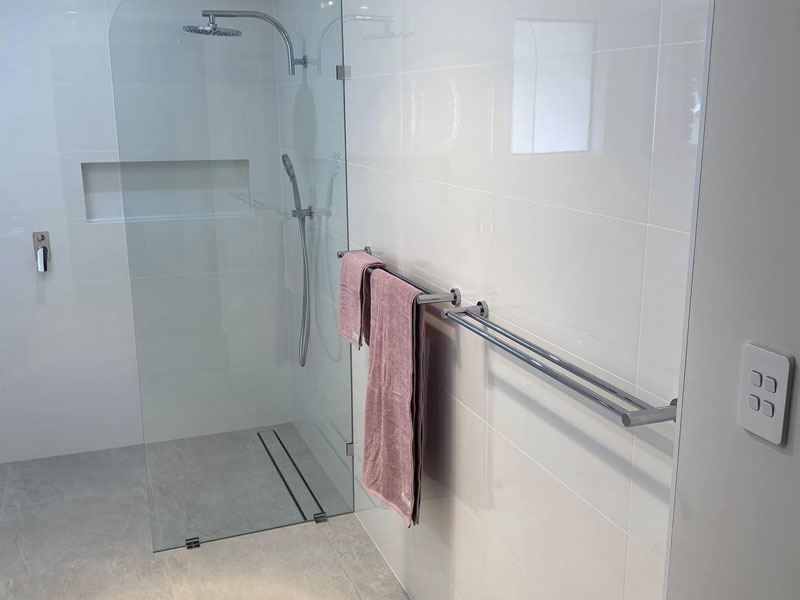 Frameless glass shower with rain shower head and chrome towel rails