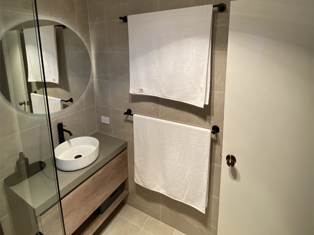 Bathroom after renovation: timber-look vanity, round backlit mirror and black towel rails
