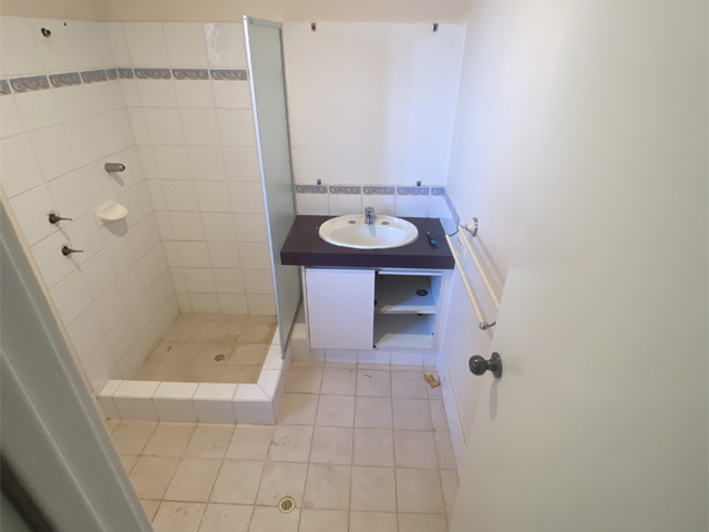 Bathroom before renovation: tiled shower recess and small vanity with dark top
