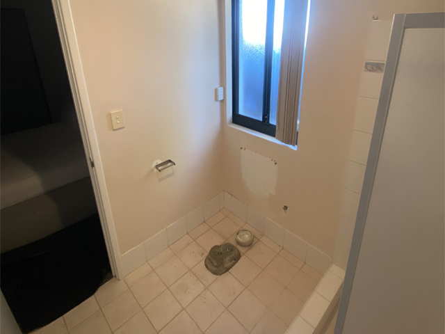 Bathroom before renovation: old floor tiles and bare walls with fittings removed
