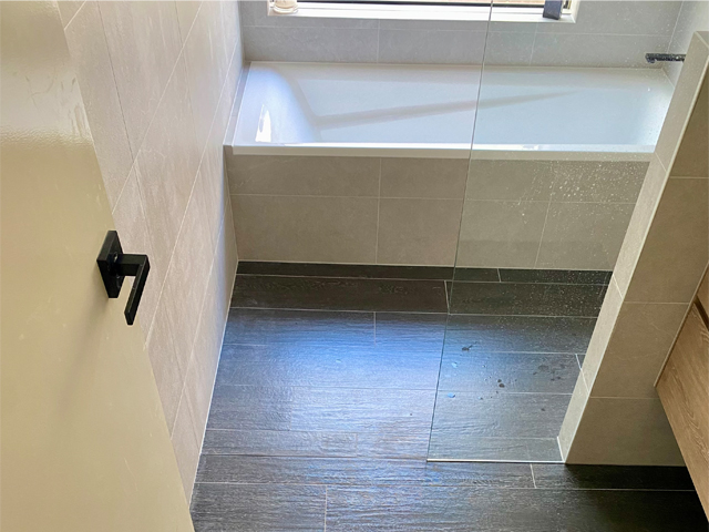 Bathroom after renovation: bath and walk-in shower with dark plank-look floor tiles