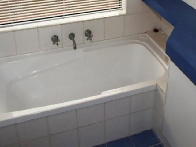 Bathroom before renovation: white bath with dated tiles and blue benchtop