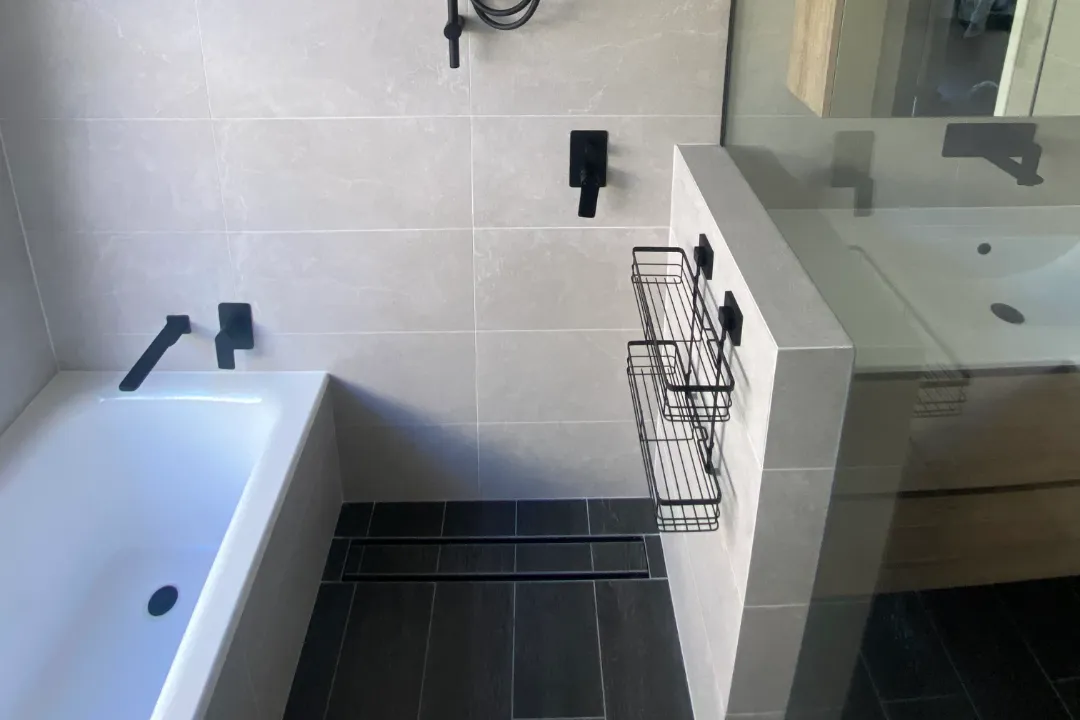 Small Bathroom Renovations Built-in bath beside a walk-in shower with black tapware and dark floor tiles