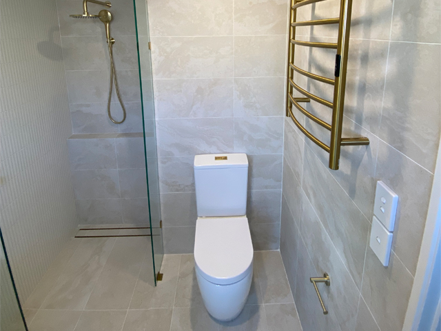 Same space after renovation: walk-in shower, toilet and brass heated towel rail