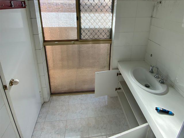 Bathroom before renovation: long white vanity, old floor tiles and frosted window