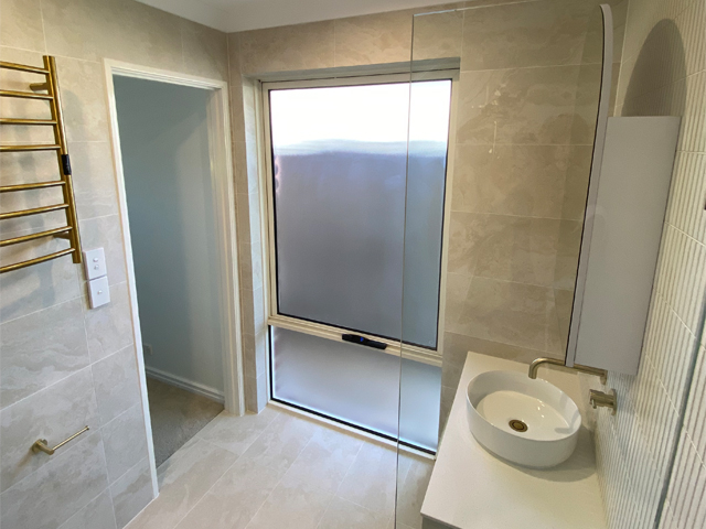 Same bathroom after renovation: walk-in shower, round basin and brass towel rail