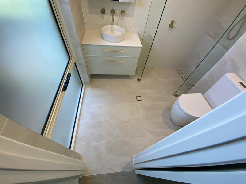 Wide-angle view of a tiled bathroom with toilet, vanity and frosted window