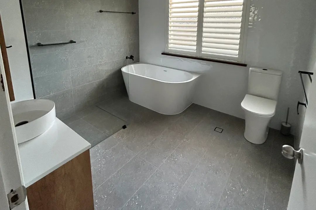 Bathroom Renovations Bayswater Bathroom with freestanding bath, toilet and grey floor tiles below a shuttered window