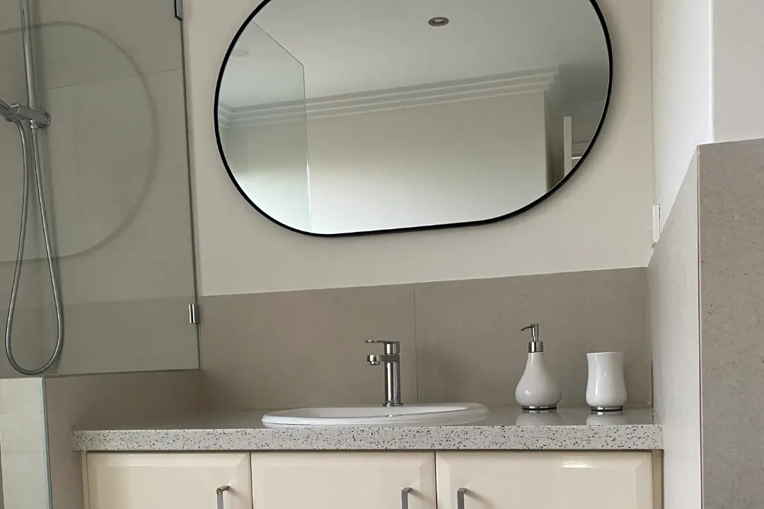 Bathroom Renovations Woodvale Inset basin on a speckled stone vanity top below a black-framed oval mirror