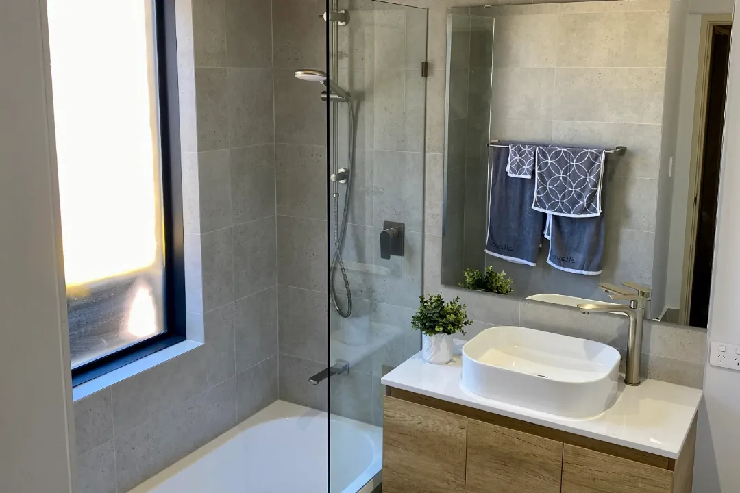 Bathroom Renovations Woodvale Bath with glass shower screen beside a timber-look vanity and wall mirror