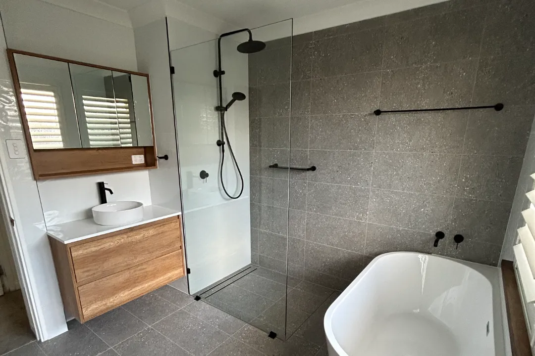 Bathroom Renovations Ellenbrook Grey-tiled bathroom with rain shower, black tapware, bath and mirror cabinet