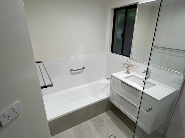 Same bathroom after renovation: white bath, white vanity and pale tiles