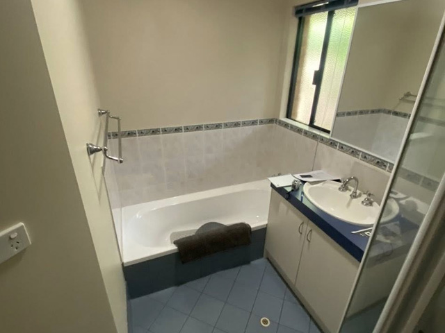 Bathroom before renovation: blue floor tiles, old bath and dark vanity top
