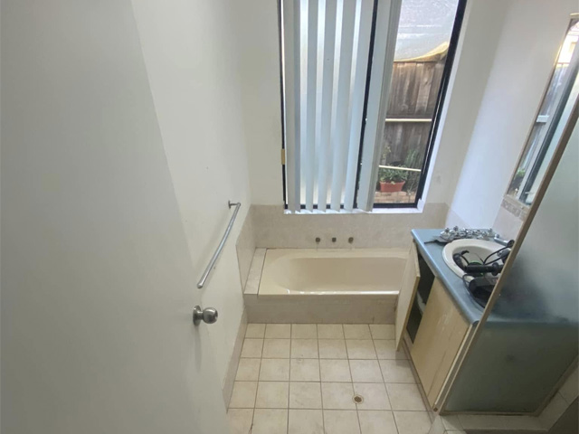 Bathroom before renovation: cream bath, beige floor tiles and dated vanity