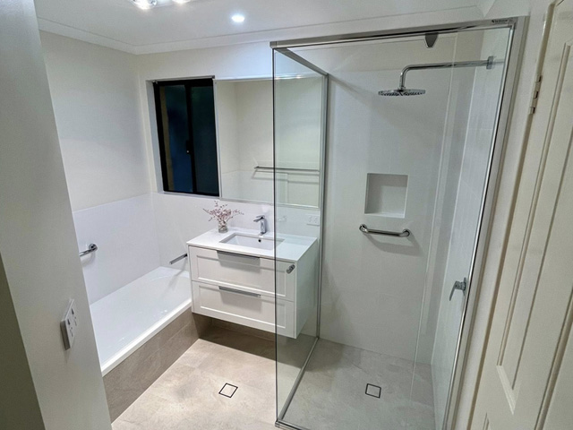 Bright bathroom with built-in bath, white vanity and glass shower screen