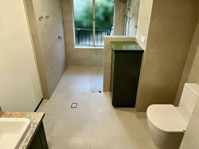 Tiled bathroom with green vanity, toilet and walk-in shower by a window