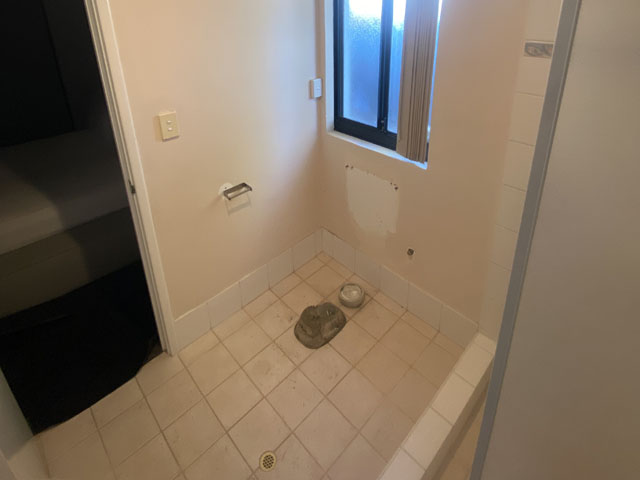 Bathroom before renovation: old floor tiles and bare walls with fittings removed