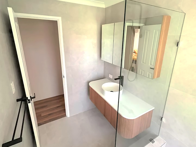 Same bathroom after renovation: curved fluted vanity, mirror cabinet and glass shower