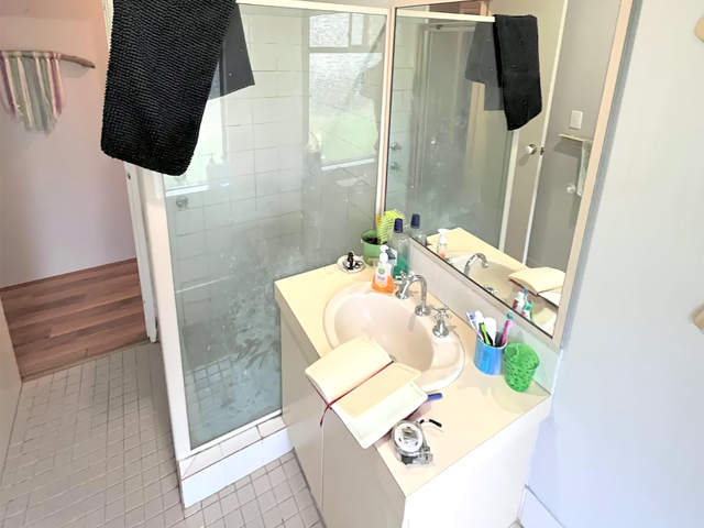 Bathroom before renovation: framed shower, cluttered vanity and small floor tiles
