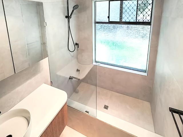 Same bathroom after renovation: walk-in shower with glass screen and fluted vanity