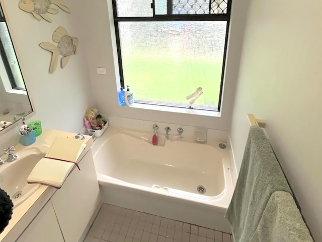 Bathroom before renovation: cream bath, old vanity and small floor tiles
